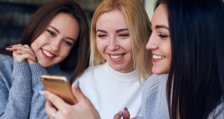 three young beautiful women using mobile phone at cafe