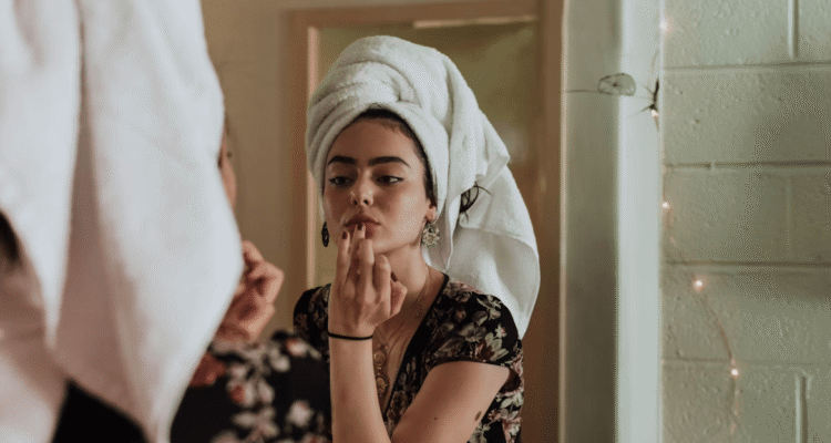 Woman with towel on head looking in mirror reflecting on beauty enhancements
